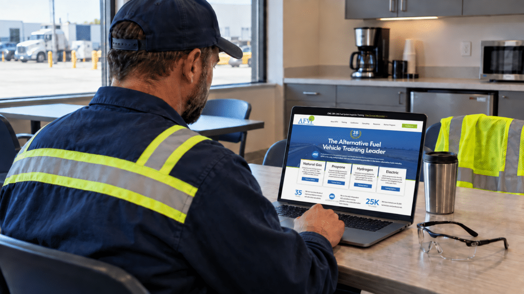 A technician in a high-visibility work shirt reviewing alternative fuel vehicle training on a laptop in a breakroom.